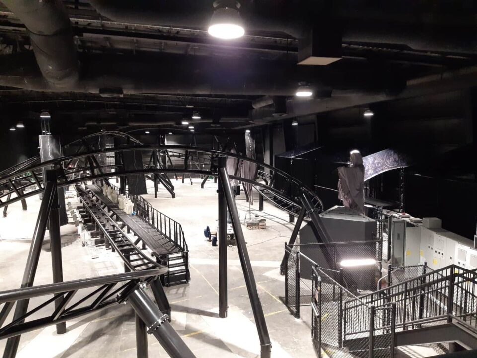 Innenaufnahme eines Freizeitparks, die ein komplexes Achterbahnsystem mit schwarzen Schienen zeigt.